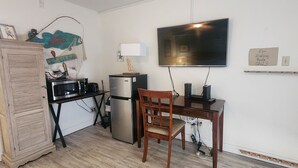 A compact kitchen with a refrigerator, microwave, and a dining table with a chair. A television is mounted on the wall above the table. - Spring Pricing at Seaside Bungalow (Rockport)