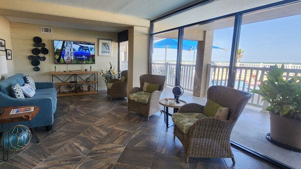 A spacious balcony with wicker furniture, a flat-screen TV, and a view of the ocean. - Spring Pricing at Seaside Bungalow (Rockport)
