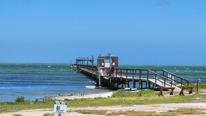 A pier extending into a body of water with a small structure at the end. - Spring Pricing at Seaside Bungalow (Rockport)