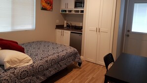 Ein gemütliches Schlafzimmer mit kariertem Bett, eine kleine Küchenzeile mit Mikrowelle und eine Tür zum Badezimmer.