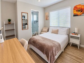 A bedroom with a bed, bedside table, chair, and a view of the bathroom.
