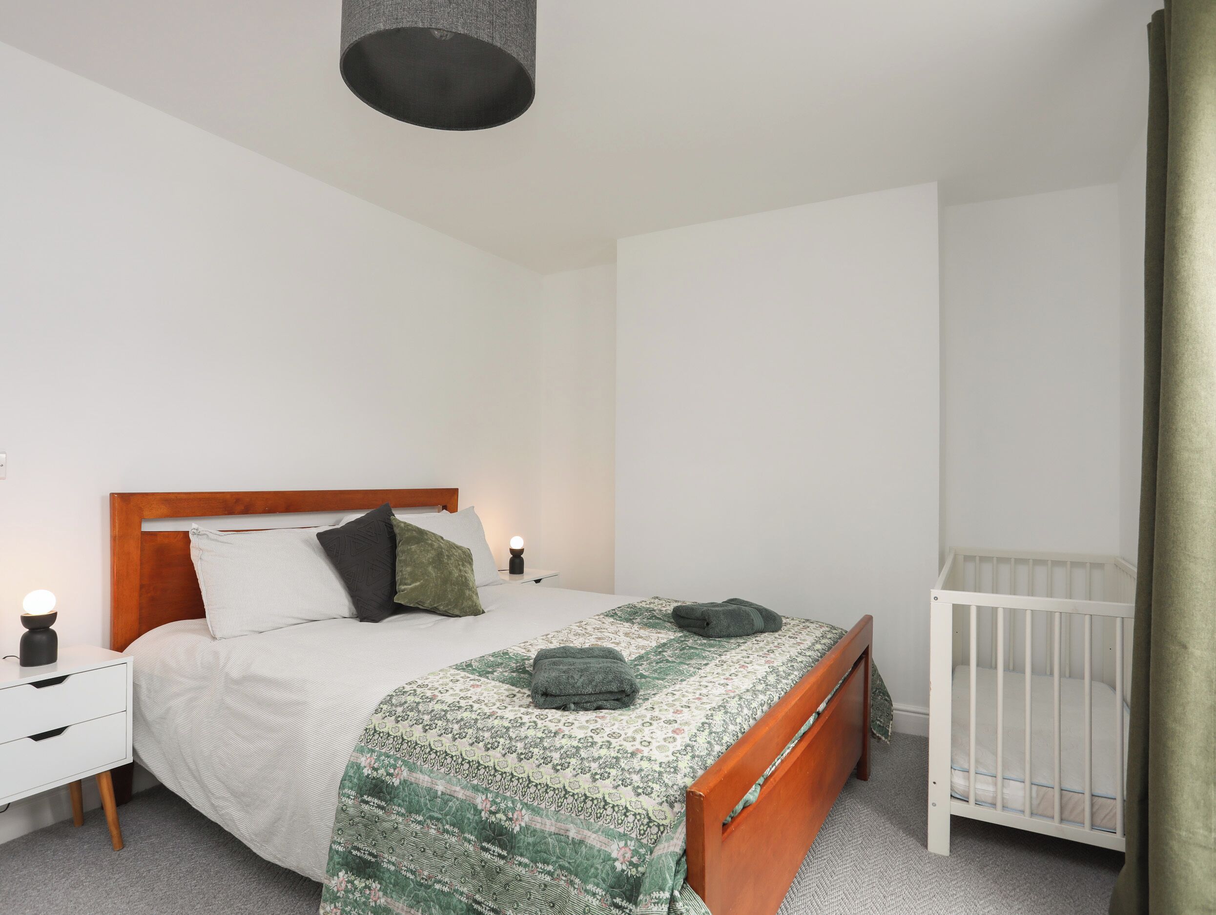 Ein Schlafzimmer mit einem hölzernen Bett, weißen Nachttischen, einer Nachttischlampe und einem Babybett.
