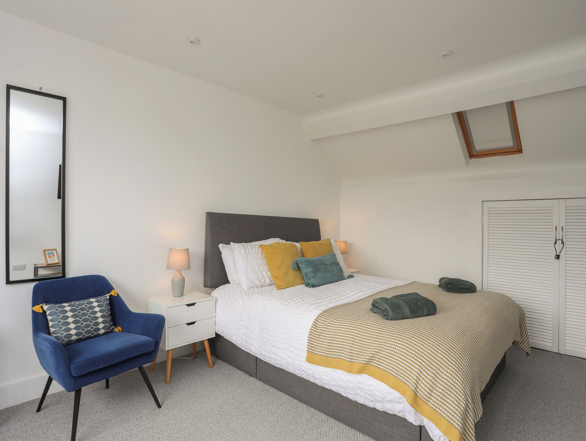 A bedroom with a bed, a chair, a nightstand, a mirror, and a wardrobe.