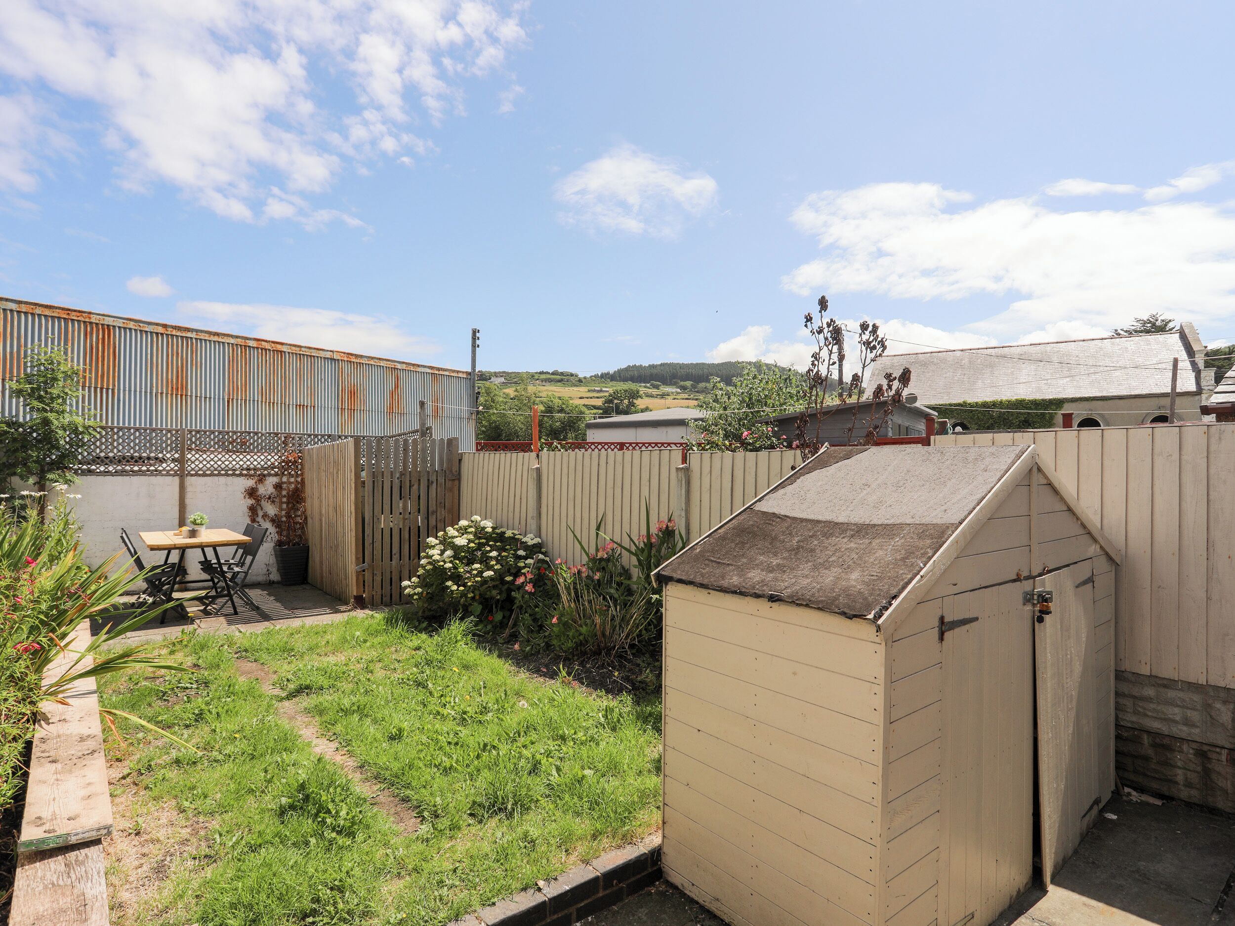 A fenced backyard with a wooden shed, a table with chairs, and a small garden area.