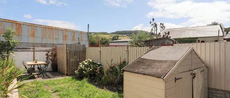 A fenced backyard with a wooden shed, a table with chairs, and a small garden area.