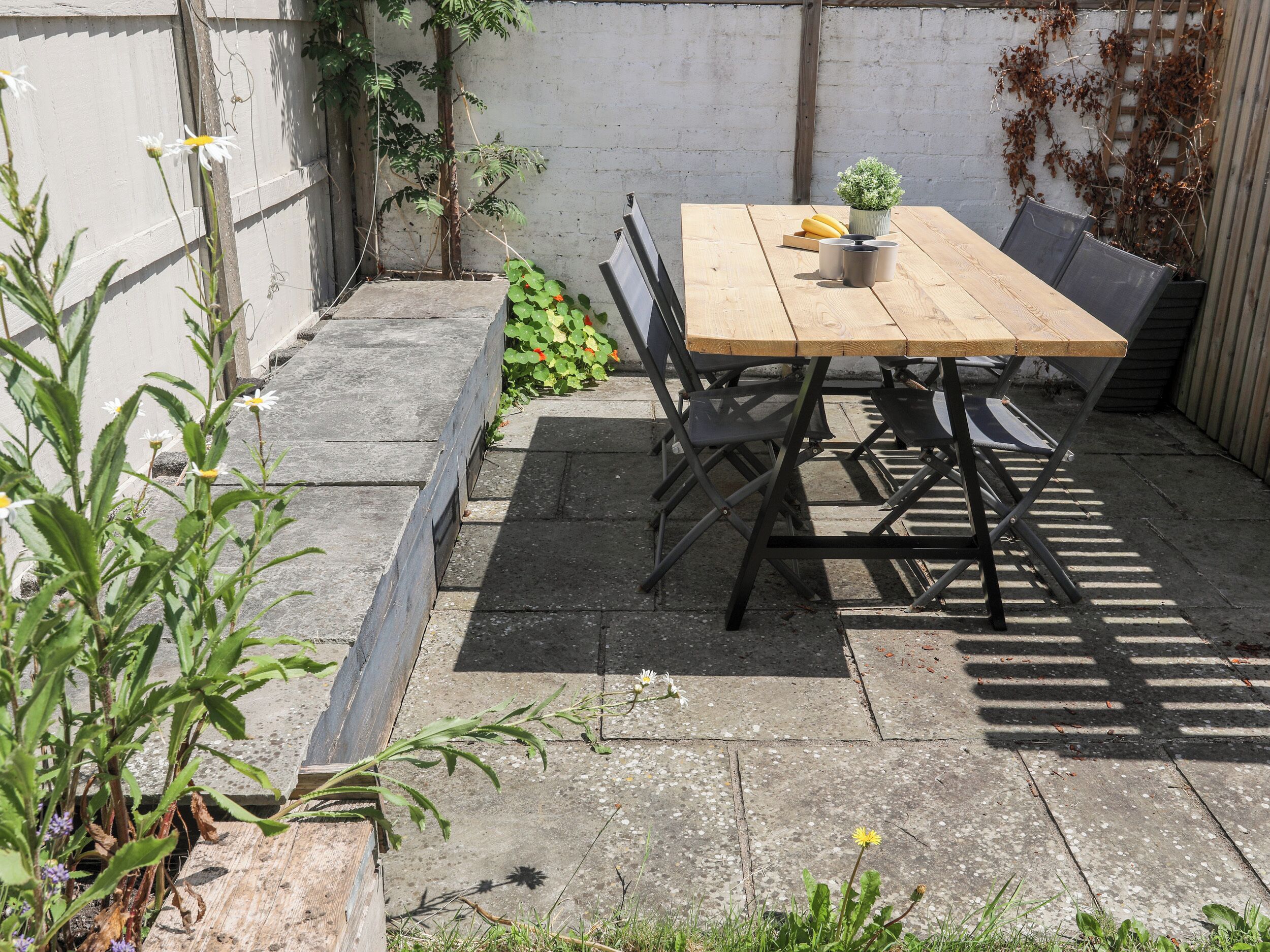 A wooden table with chairs, a potted plant, and a small table with cups and bananas.