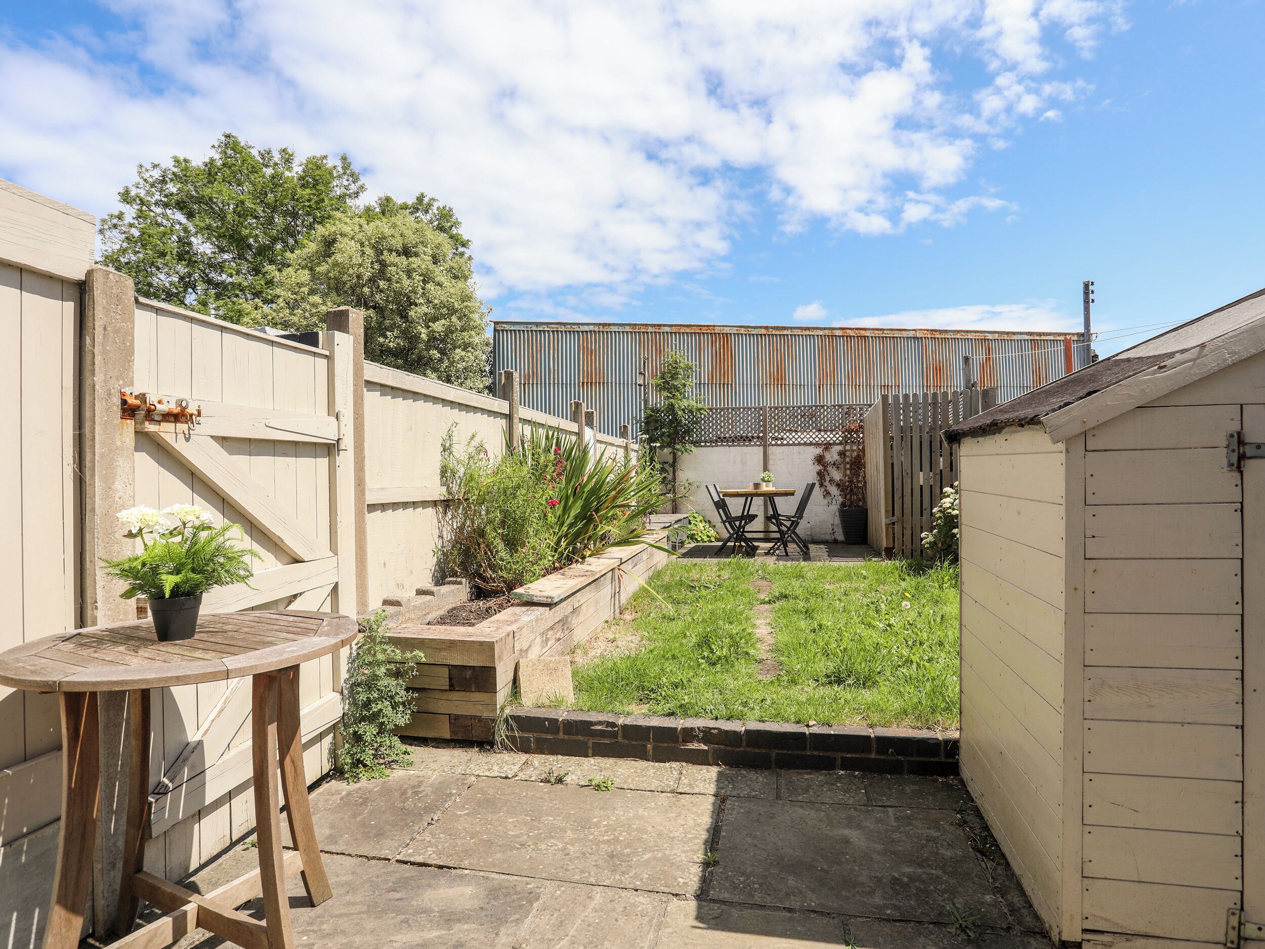 A small backyard with a wooden table and chairs, a potted plant, and a fenced area.