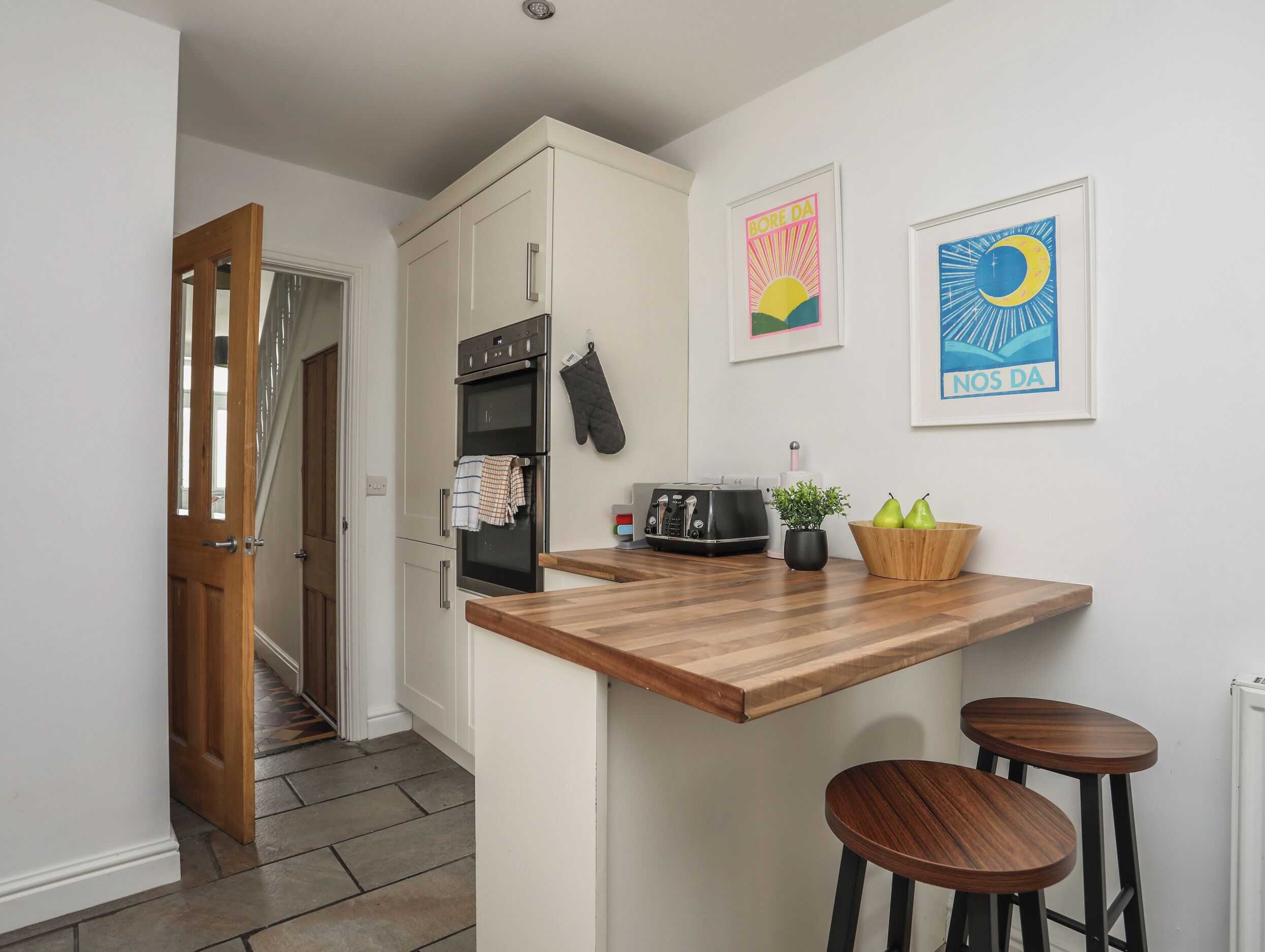 A compact kitchen with a wooden countertop, a toaster, a kettle, and a small plant.