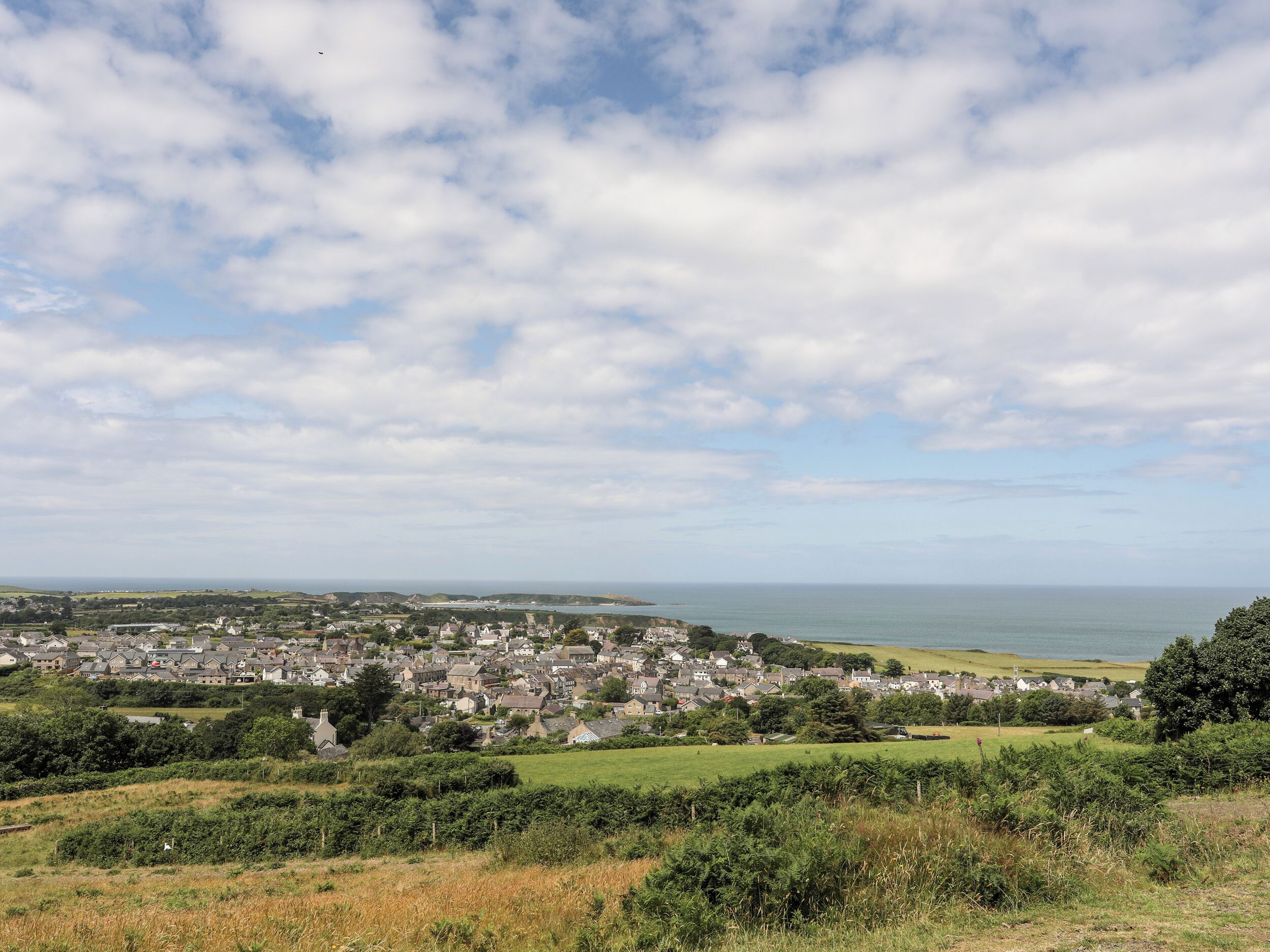 A coastal town with a mix of residential and commercial buildings, a clear view of the sea, and a hilly landscape.