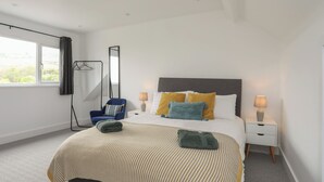 A modern bedroom with a large bed, bedside lamps, a chair, and a mirror. - Maes Y Ddol (Pwllheli)