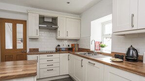 A modern kitchen with white cabinets, a wooden countertop, a stainless steel sink, and a kettle. - Maes Y Ddol (Pwllheli)