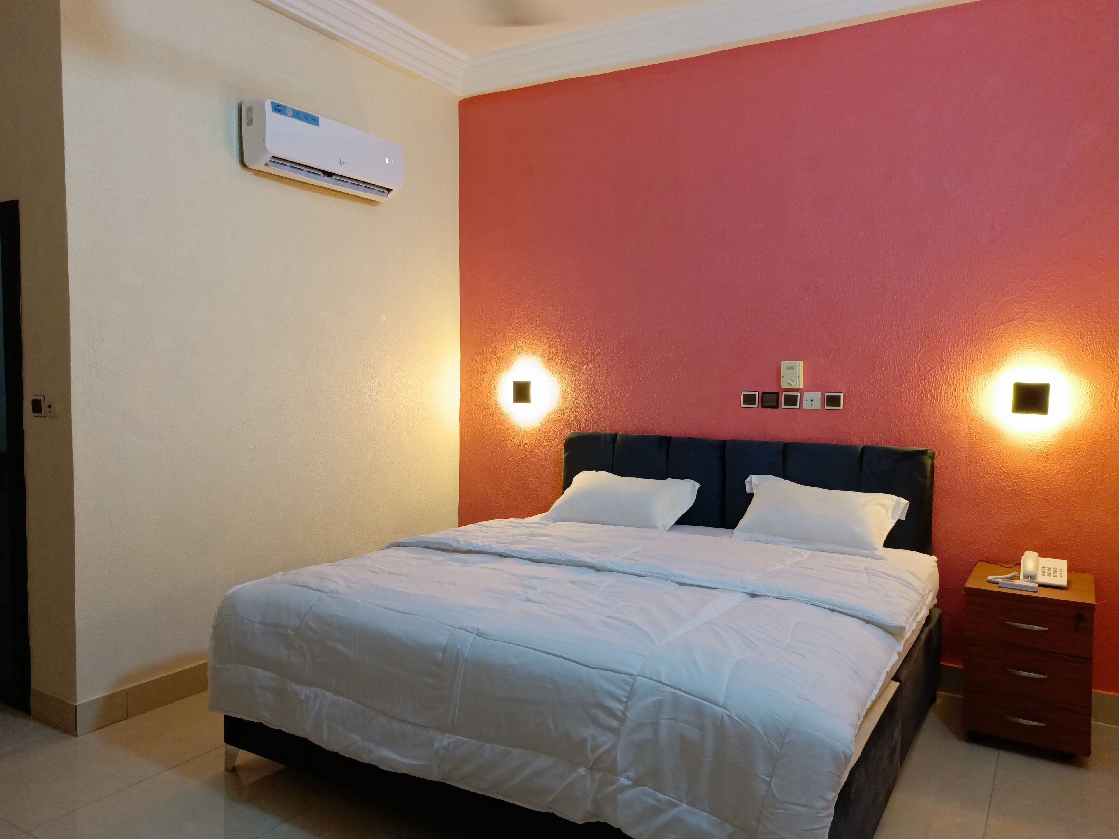 Una habitación de hotel con cama, mesita de noche y un equipo de aire acondicionado en la pared.