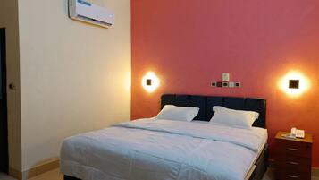 Una habitación de hotel con cama, mesita de noche y un equipo de aire acondicionado en la pared.