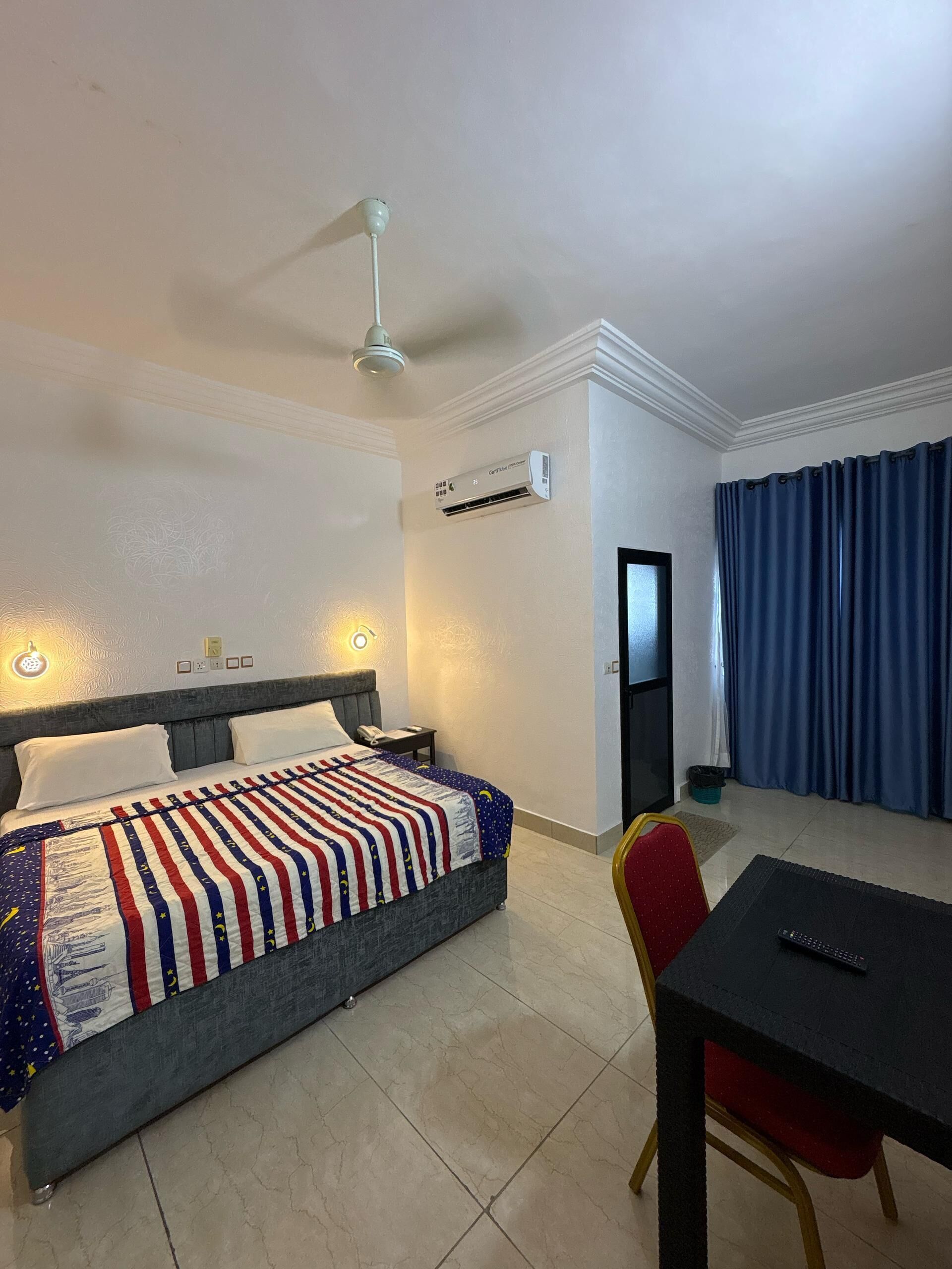 Habitación de hotel con cama, escritorio, silla, aire acondicionado y puerta.