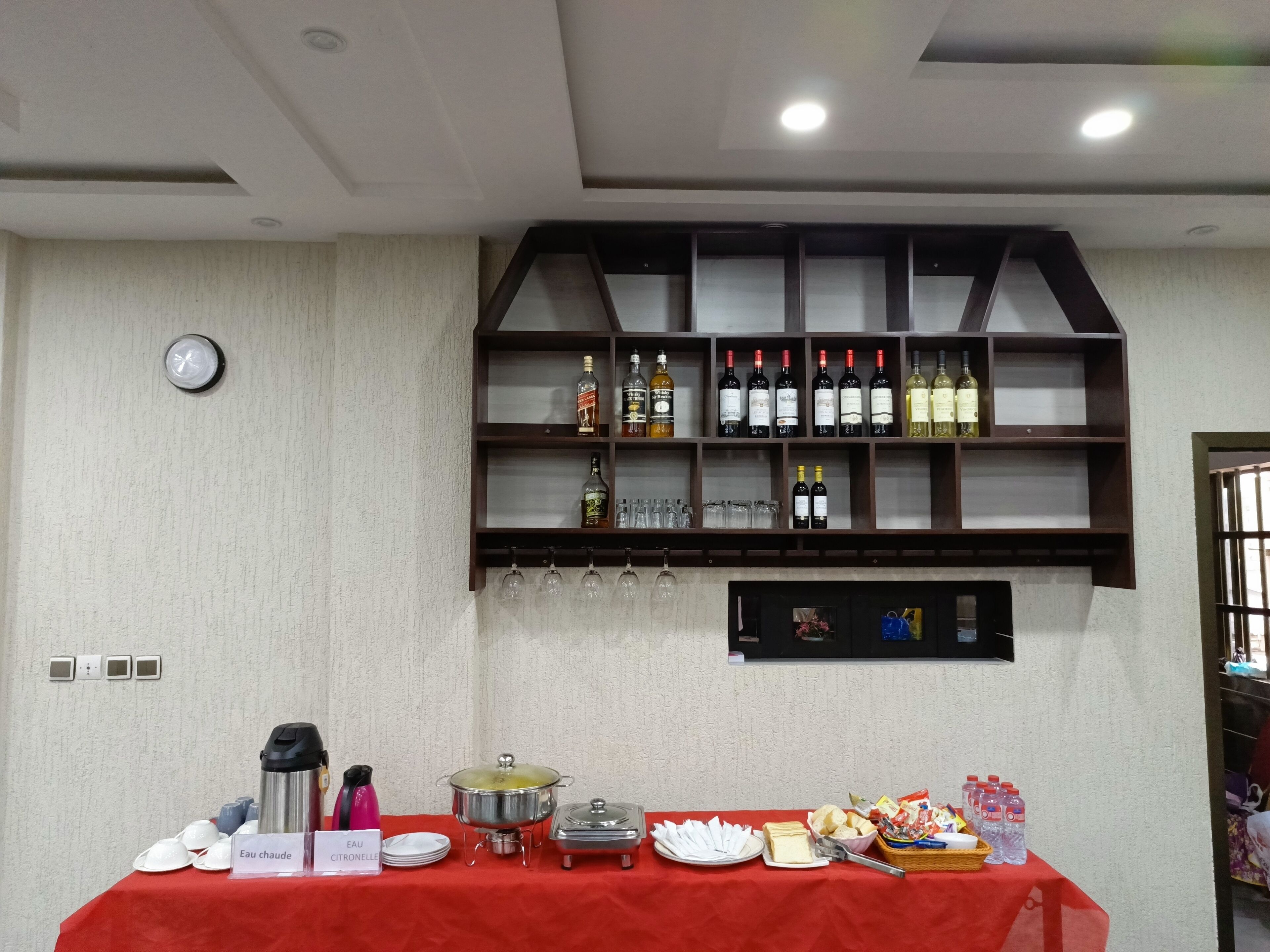 A buffet setup with a red tablecloth, a variety of beverages, and food items.