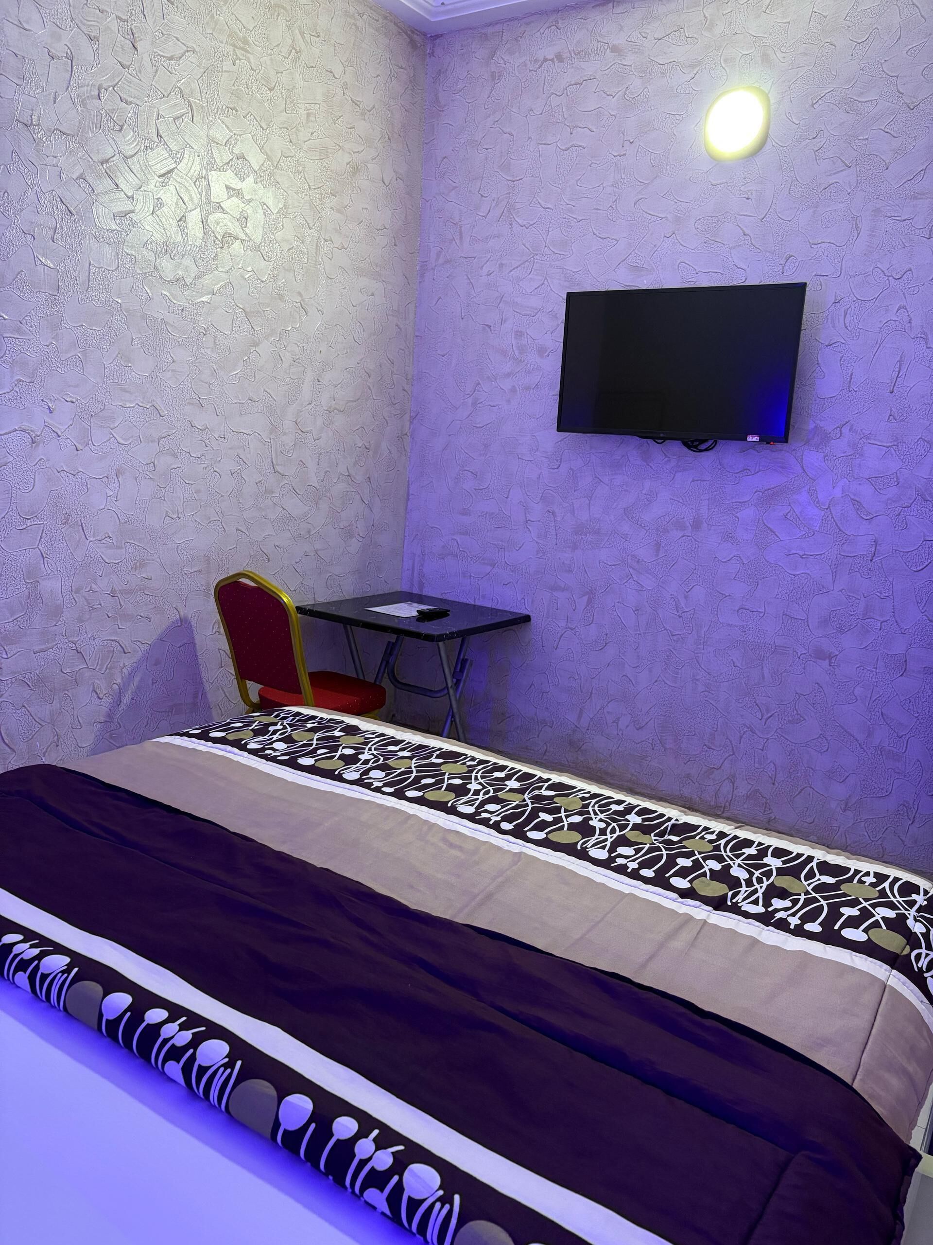 Ein Zimmer mit einem Bett, einem Schreibtisch, einem Sessel und einem an der Wand befestigten Fernseher.