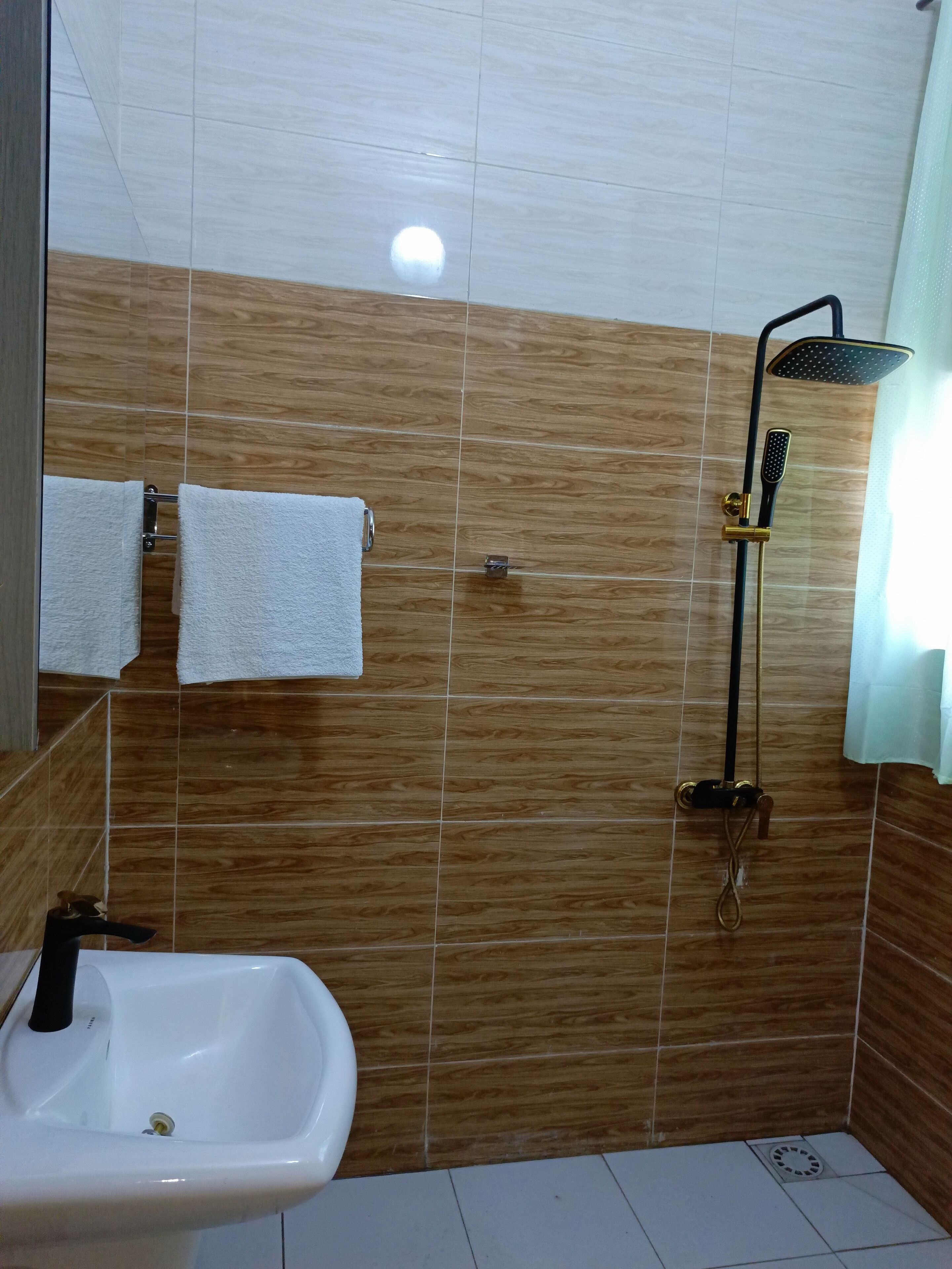 A bathroom with a white sink, a shower with a handheld showerhead, and two towels hanging on a rack.