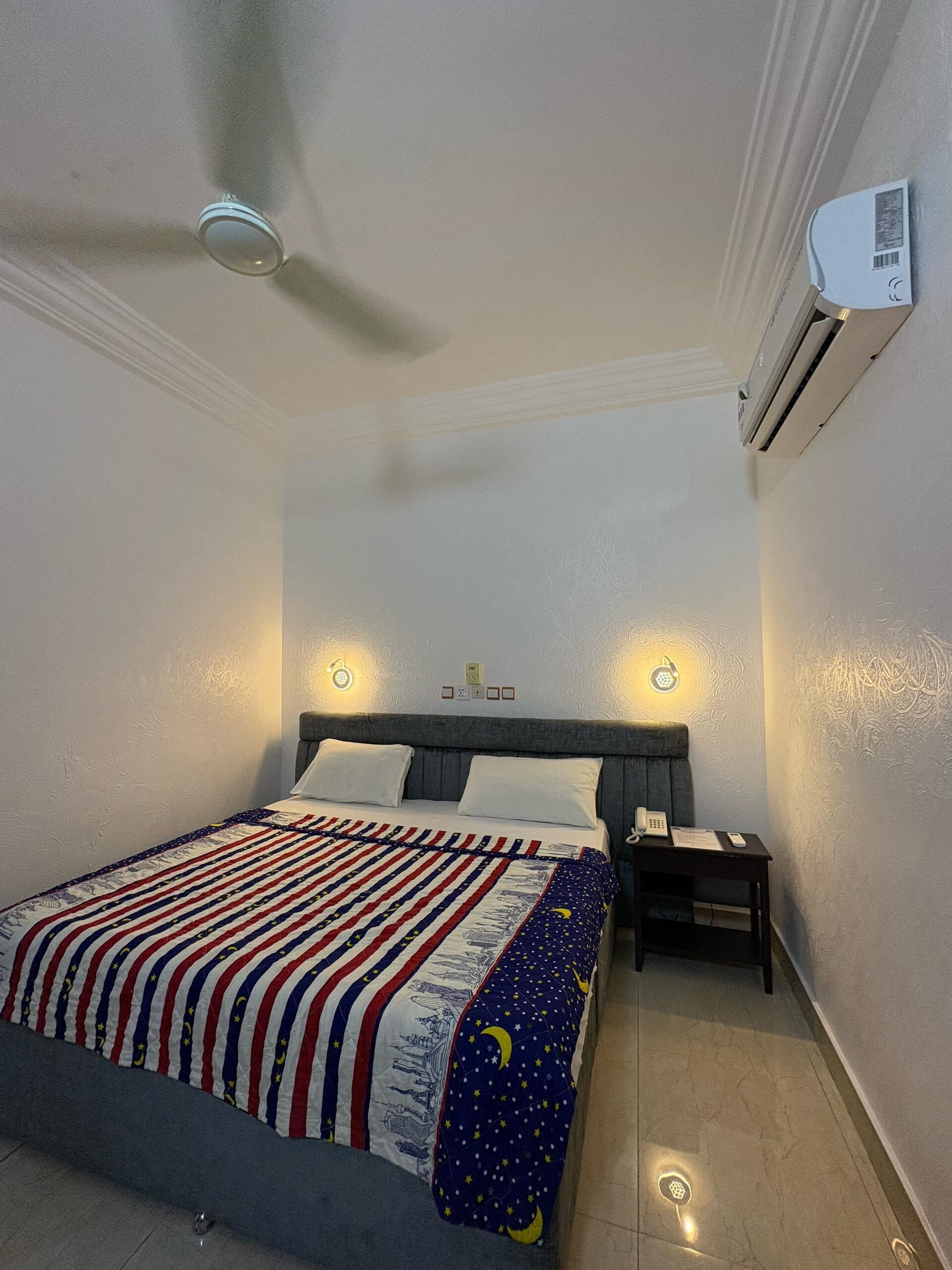 A bedroom with a bed, bedside tables, a phone, and an air conditioning unit.