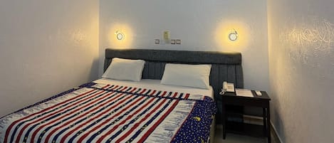 A bedroom with a bed, bedside tables, a phone, and an air conditioning unit.