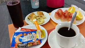 A table with food and drinks, including croissants, watermelon, lemon, coffee, and a water bottle. - HOTEL MAVILLA Cotonou (Cotonou)