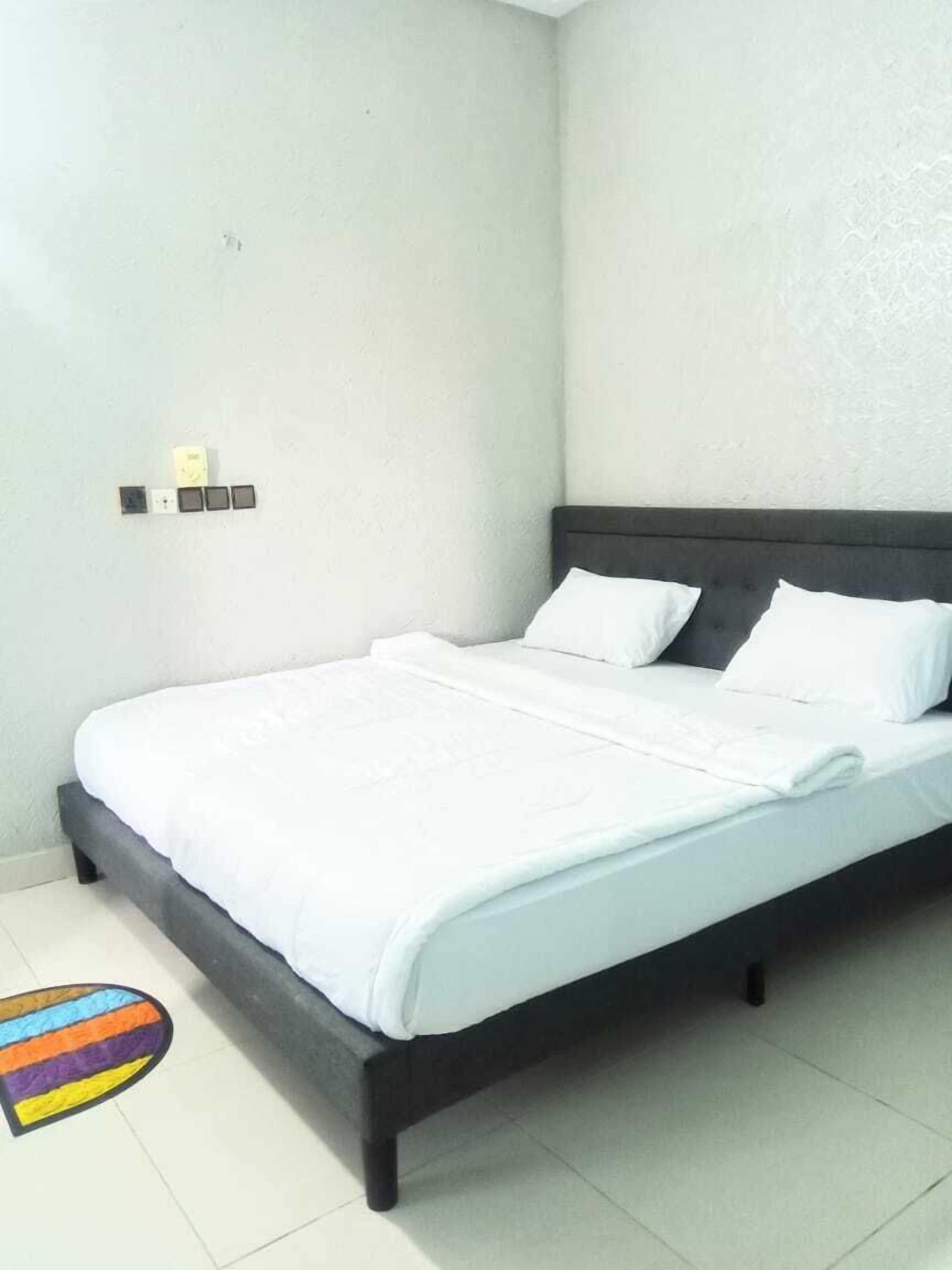 Una cama bien hecha con ropa blanca en una habitación con pared blanca lisa y suelo de baldosas.