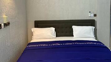 A bedroom with a bed, pillows, a blue blanket, a wall-mounted light, and a ceiling light.