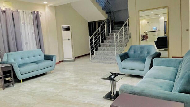 A spacious living area with a sofa, a coffee table, and a staircase leading to an upper floor. - HOTEL MAVILLA Cotonou (Cotonou)