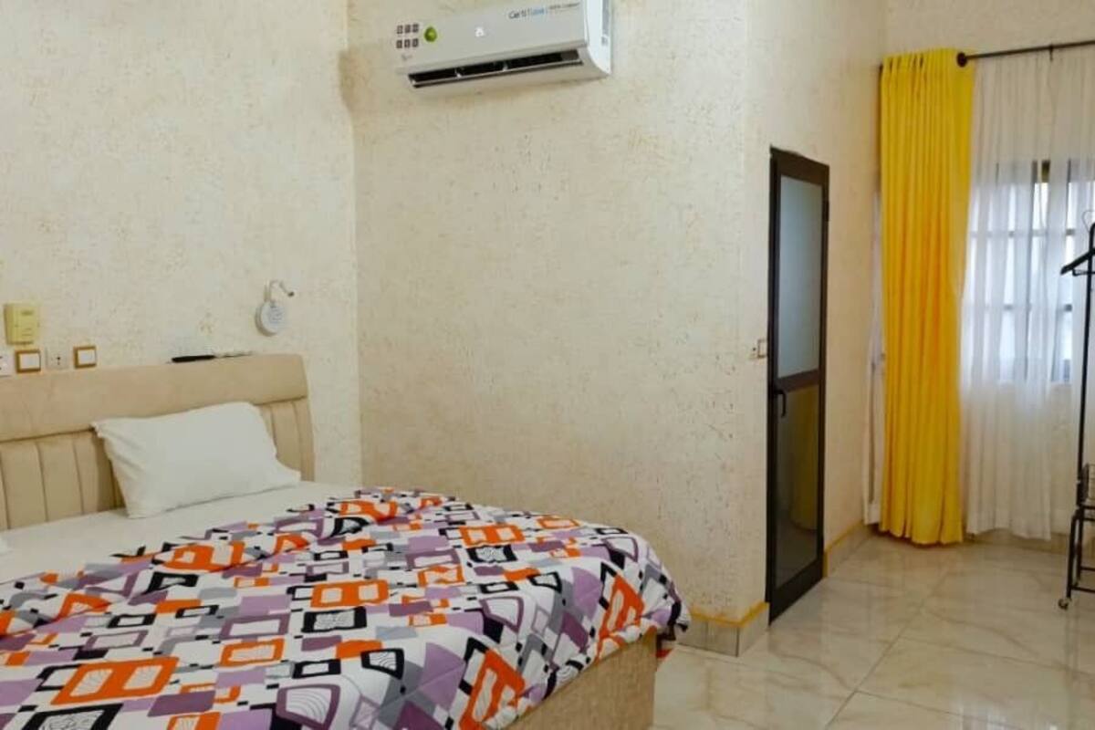Une chambre d’hôtel avec un lit, un appareil de climatisation, une porte et une fenêtre avec des rideaux jaunes.
