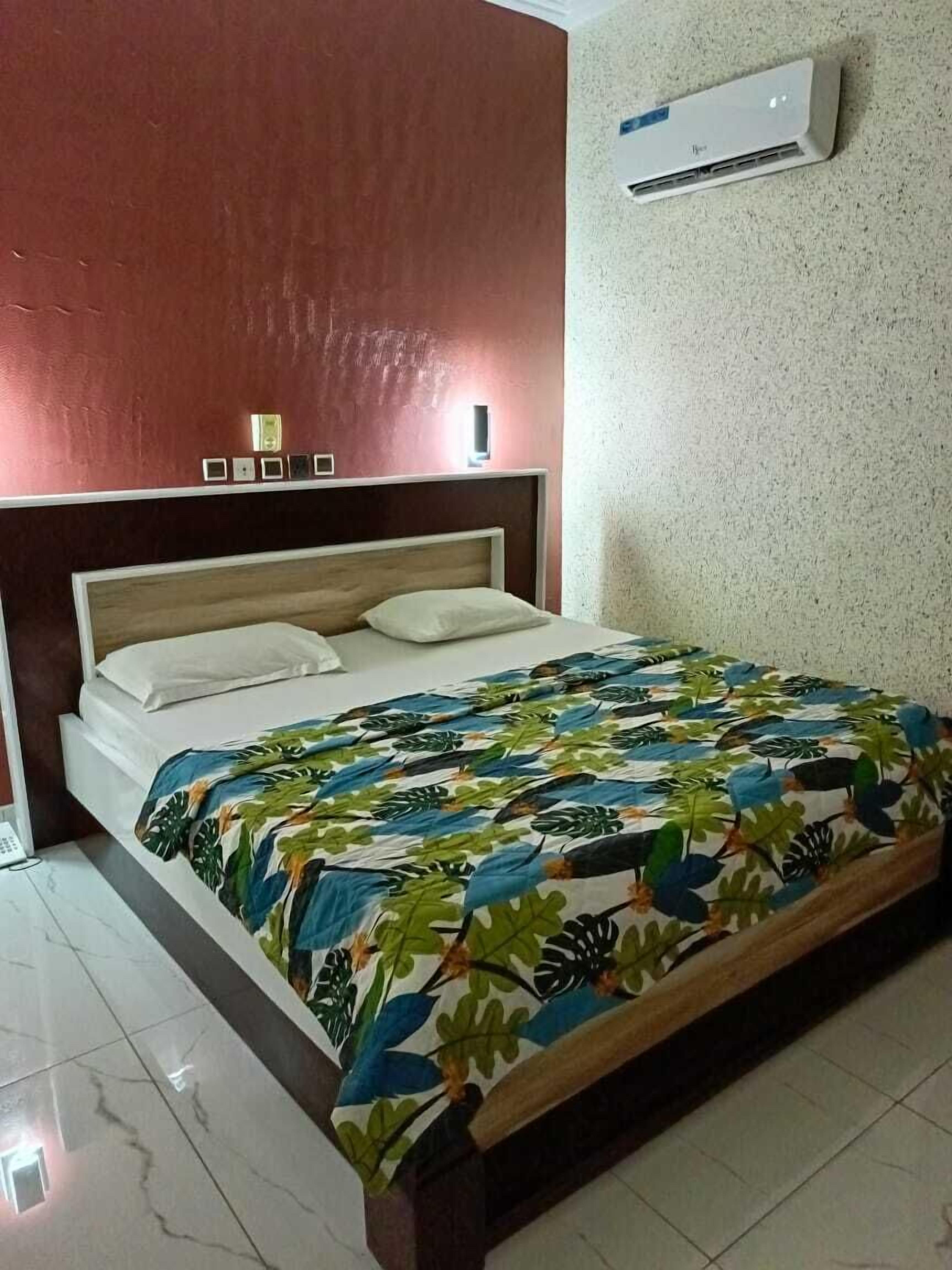 Ein Schlafzimmer mit einem Bett, einem Nachttisch, einer Wand-Klimaanlage und einer strukturierten Wand.
