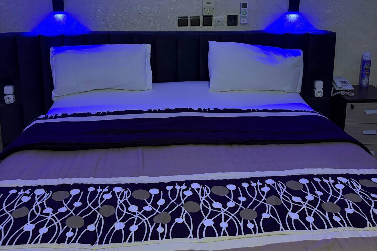 Un lit avec une couvre-lit à motifs, deux tables de chevet et des prises électriques fixées au mur.