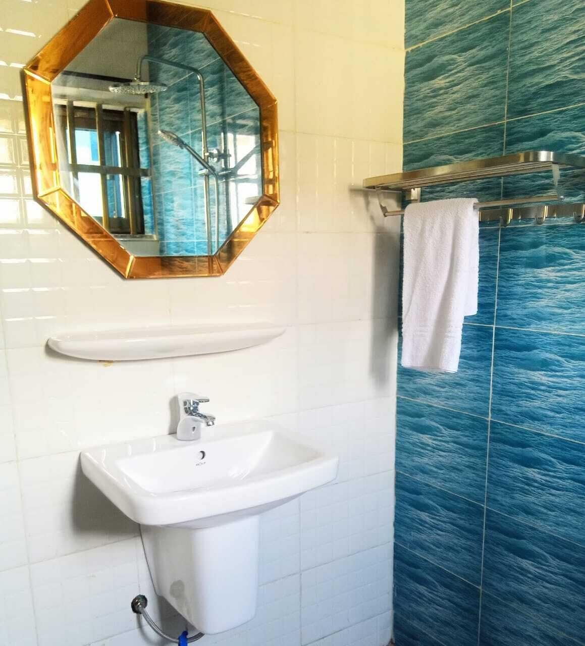 Uma casa de banho com uma pia branca, um espelho com moldura dourada e parede de chuveiro em azulejos azuis.