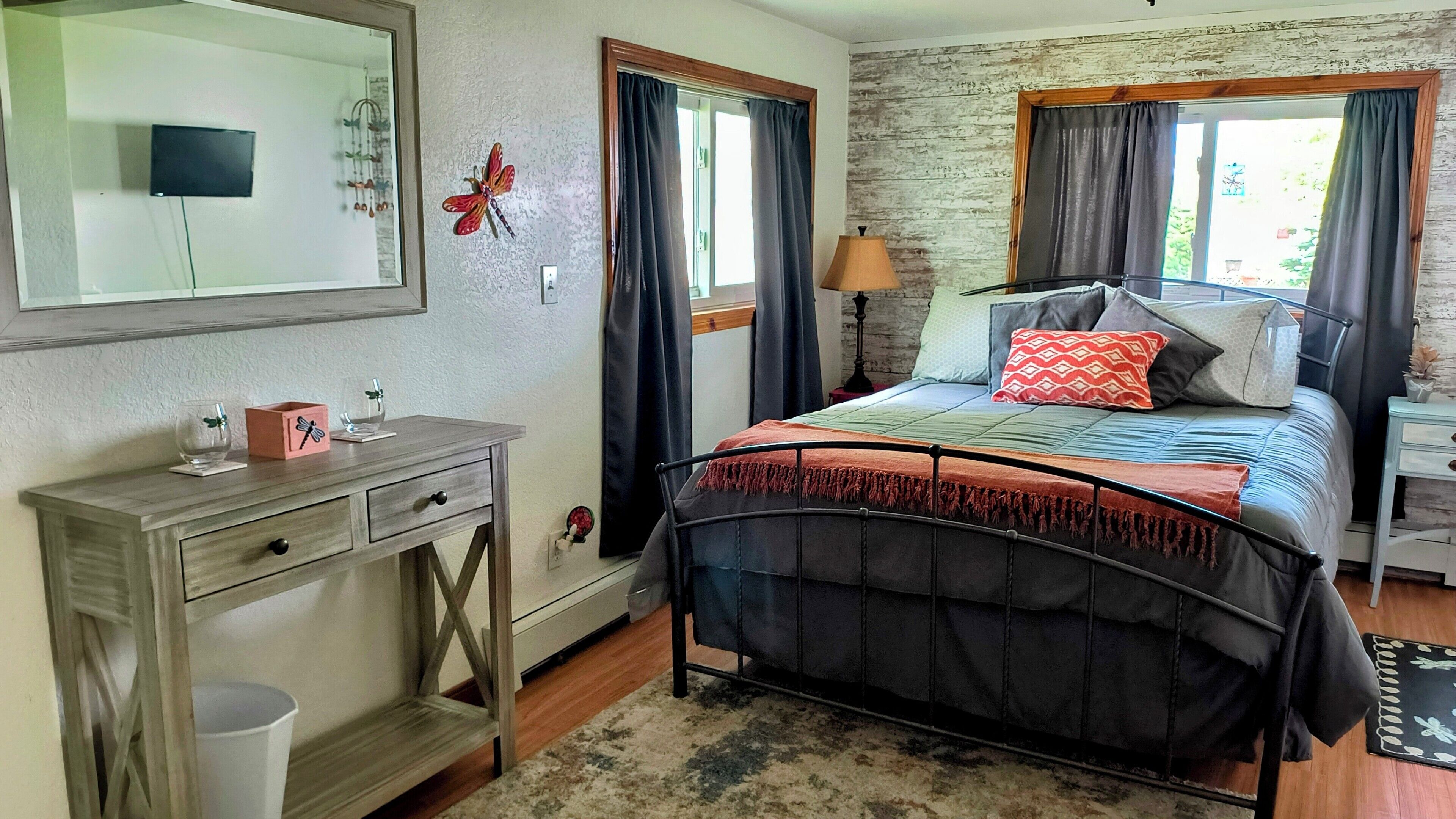 Een slaapkamer met een bed, een dressoir, een spiegel en een raam met gordijnen.