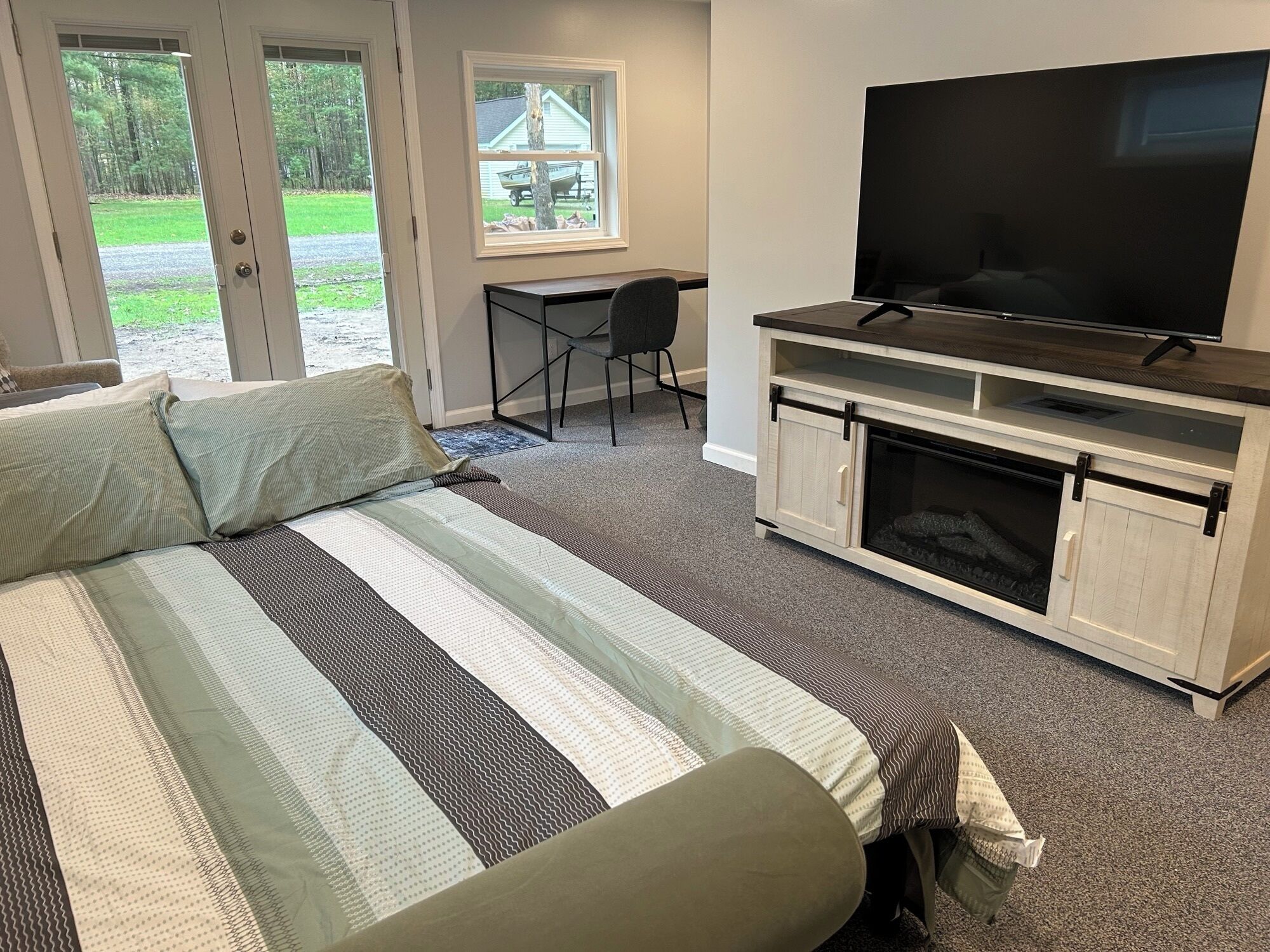 Un dormitorio con cama, televisión, chimenea y ventana con vista a una casa y un barco.