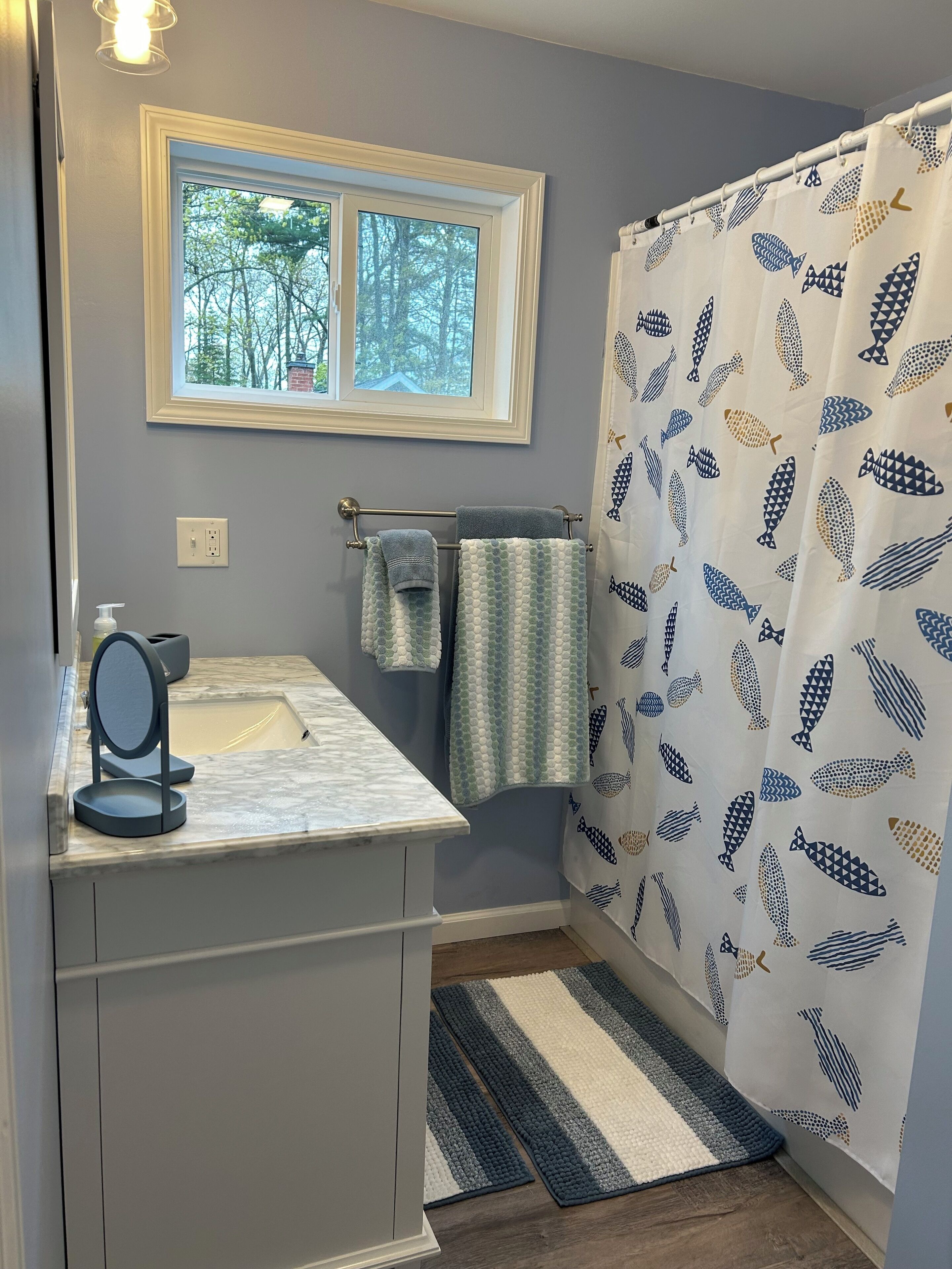 A bathroom with a sink, mirror, towel rack, and shower curtain with a fish pattern.
