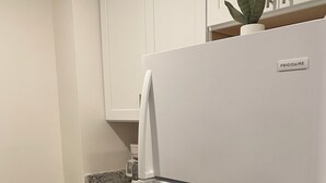 Una cocina con armarios blancos, encimera de granito, refrigerador blanco y un cubo de basura.