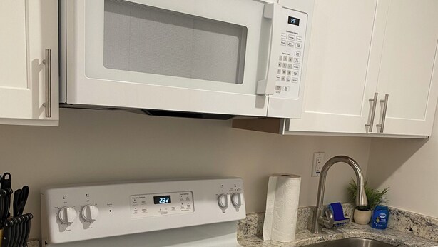 Una cocina con armarios blancos, microondas, estufa y fregadero.