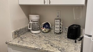 Una cocina con armarios blancos, encimera de granito, cafetera, tostadora y un tazón pequeño.