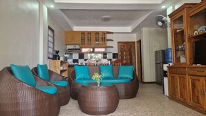 A living room with wicker furniture, a coffee table, and a kitchen in the background.