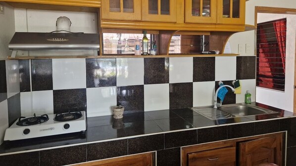 A kitchen with a gas stove, black and white checkered backsplash, wooden cabinets, and a window with red curtains.