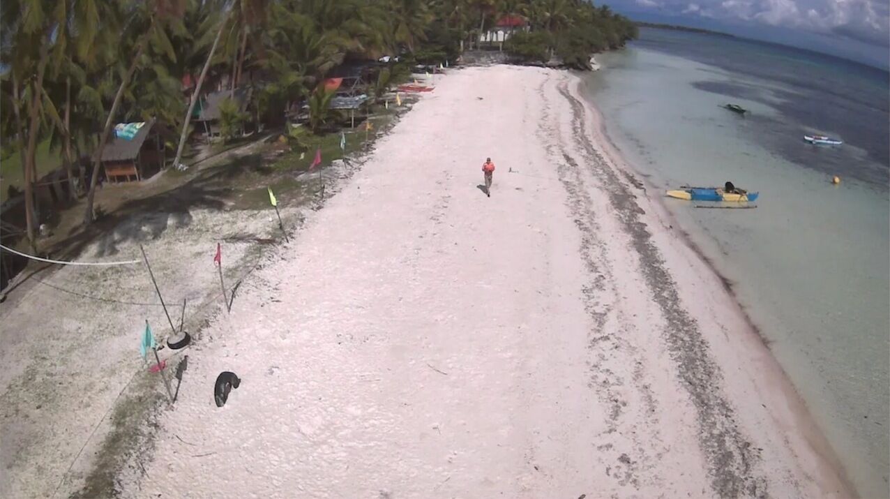 A beach with a clear path, a person walking, and a small boat on the water.