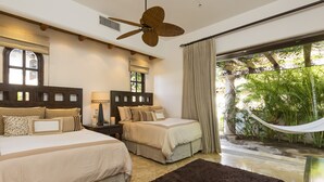 A bedroom with two beds, a ceiling fan, a large window with curtains, and a hammock outside.