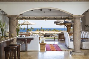 Relax in style with ocean views from this outdoor lounge, featuring a bar, seating area, and comfortable chairs.