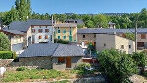 Un conjunto de casas tradicionales de piedra y enlucido con tejados inclinados, rodeado de vegetación y un cielo azul despejado.