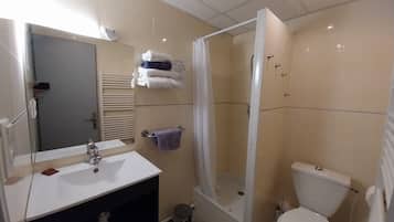 Un bany amb un lavabo blanc, un mirall i un vàter. Hi ha una zona de dutxa amb porta de vidre. Toletes penjades en un esparavell.