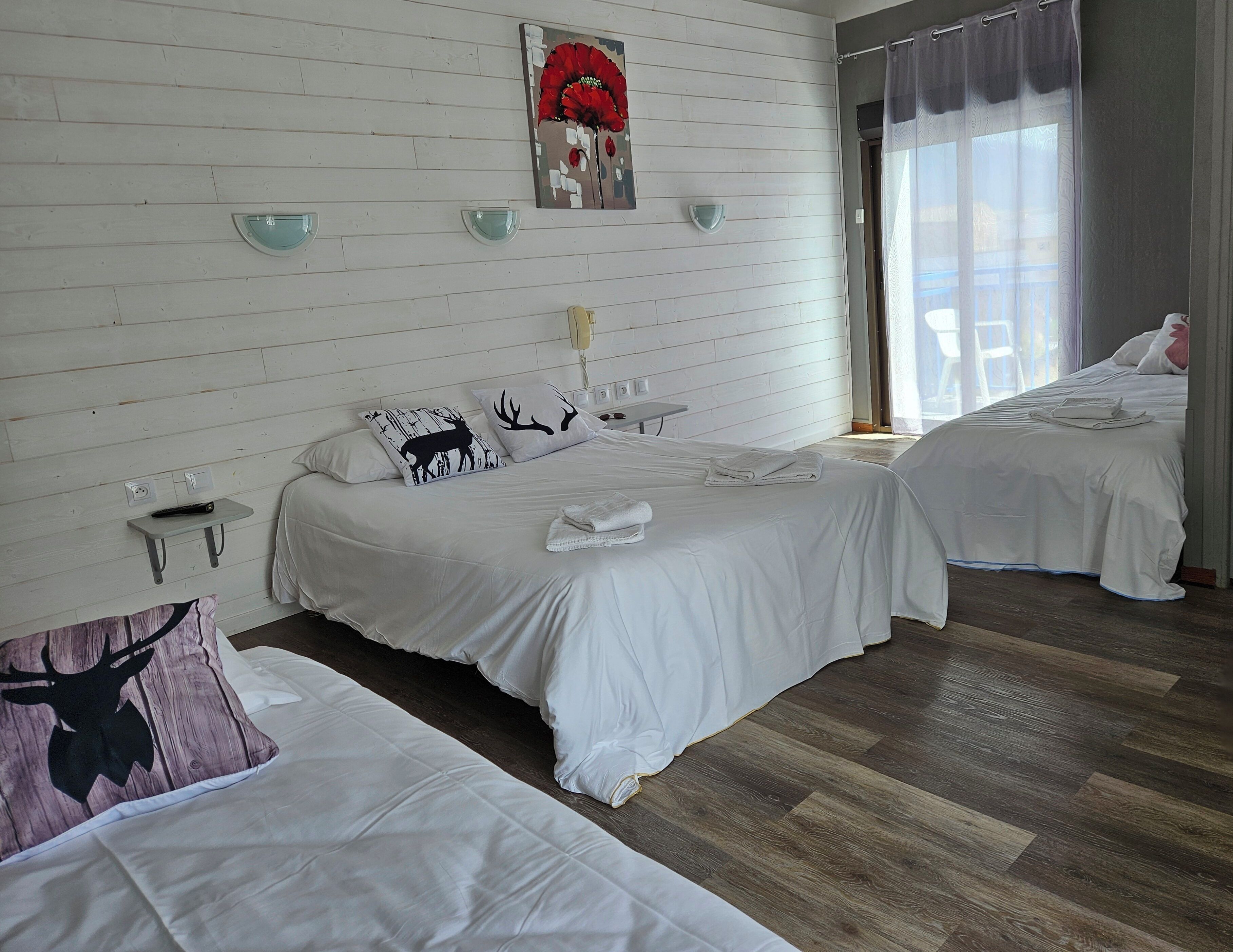 Hotelkamer met twee bedden, een houten vloer, een wandlamp en een raam met gordijnen.