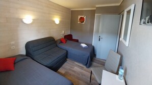 Una habitación con dos camas individuales, un sofá, una silla, un escritorio y una puerta.