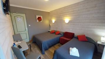 A hotel room with two beds, a desk, a chair, a TV, and a door.