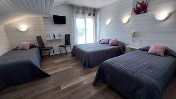 Een kamer met twee bedden, een stoel, een televisie en een raam met gordijnen.