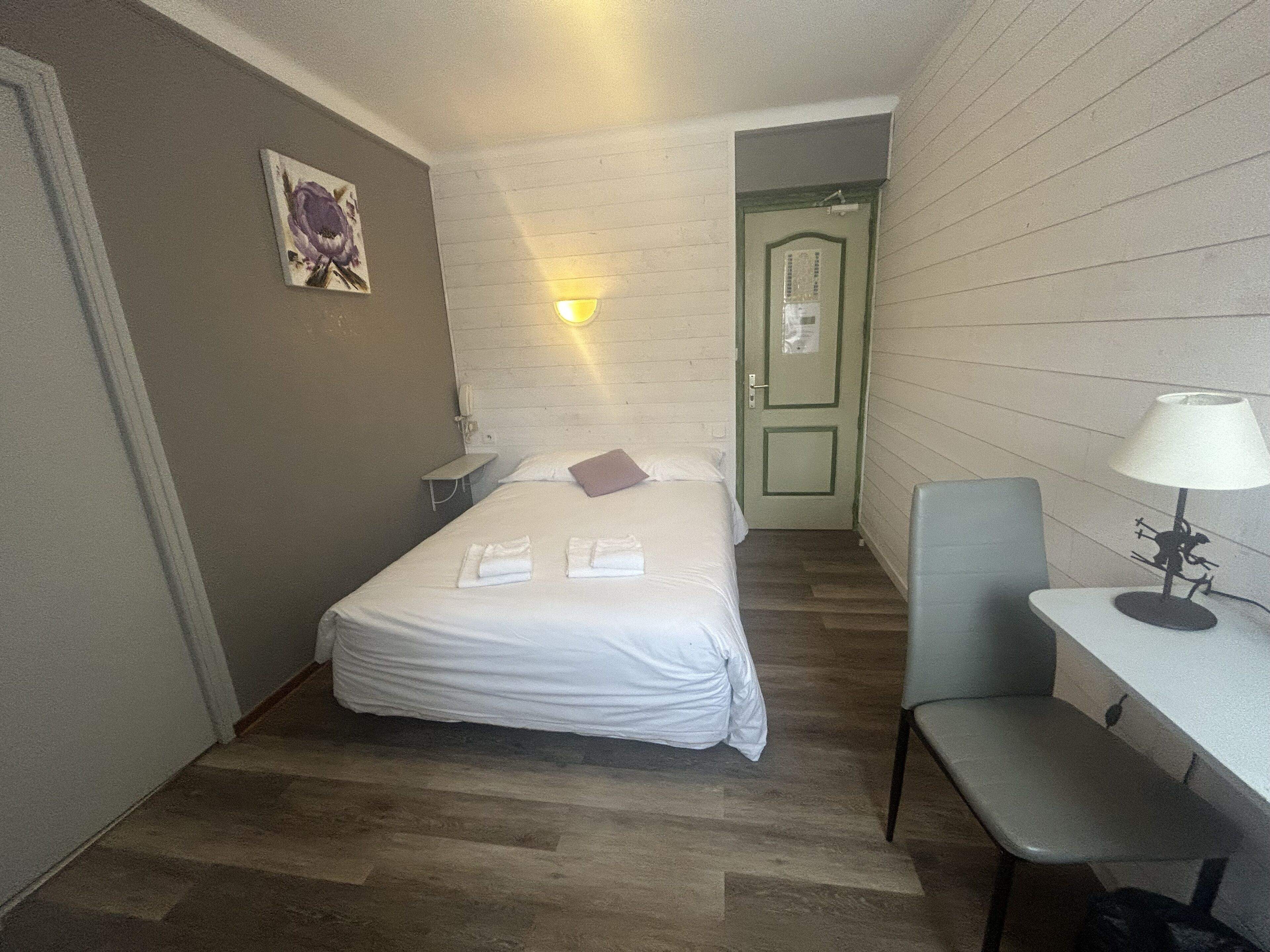 A small hotel room with a bed, a desk, a chair, and a door.