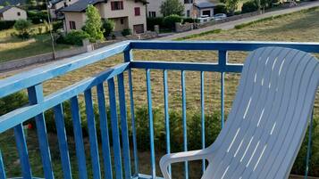 Een witte plastic stoel op een balkon met een blauwe reling, met uitzicht op een woongebied met huizen en groen.